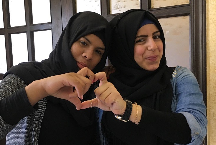 two women in hijabs making a heart sign.
