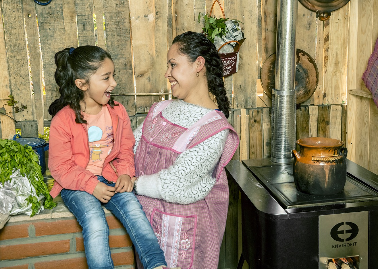 a woman and a girl standing next to a wood stove.