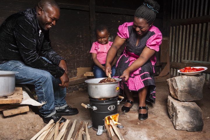 a family is cooking food on a stove in a hut.