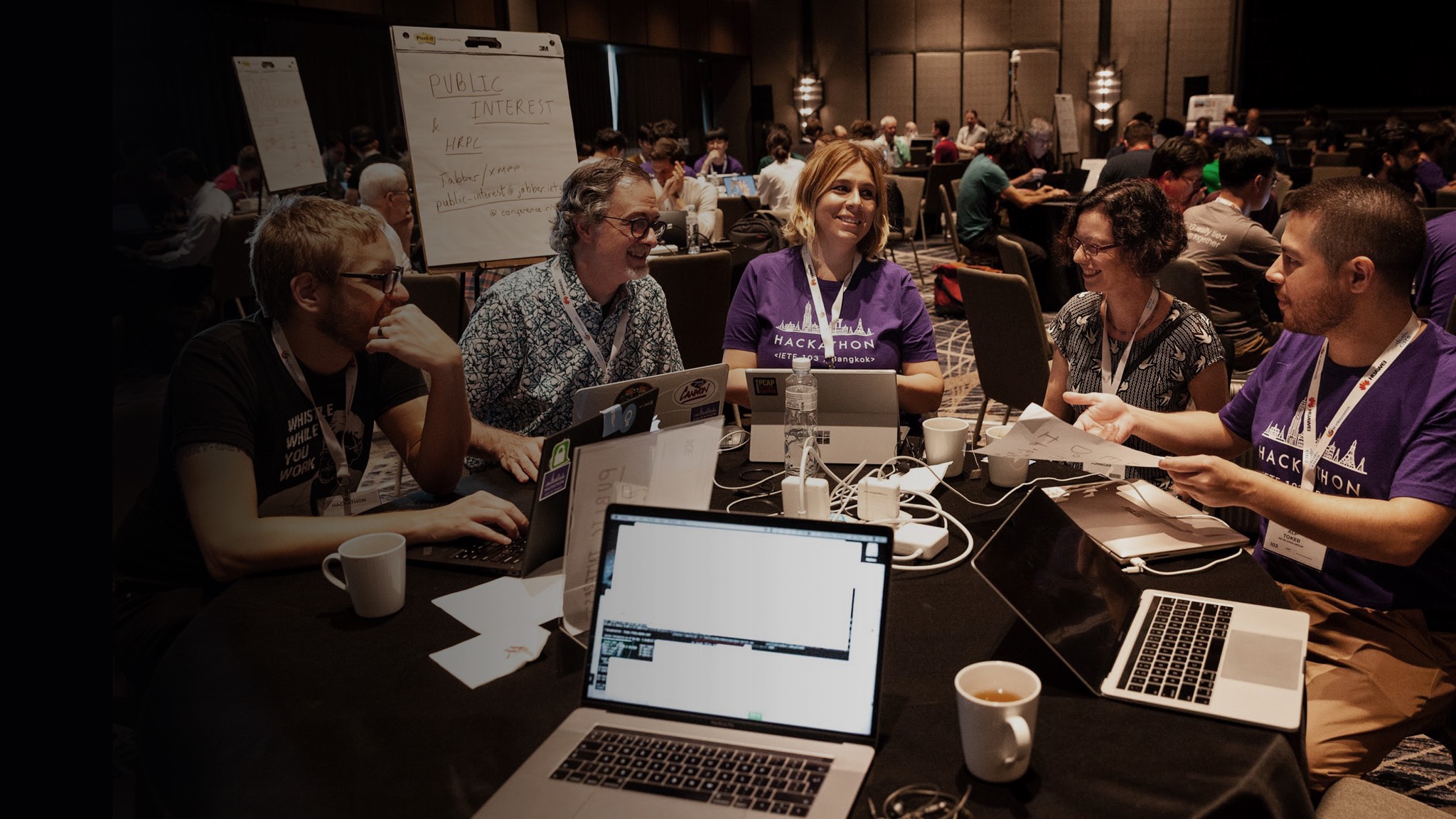 a group of people sitting around a table with laptops.