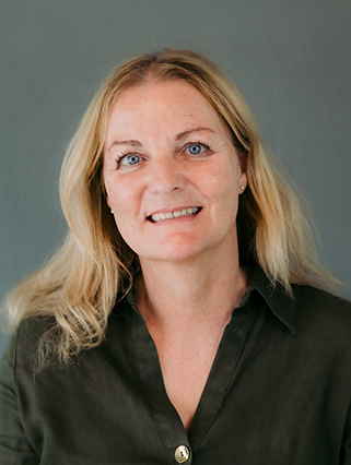 A woman with long blonde hair, wearing a dark green button-up shirt, smiles at the camera.