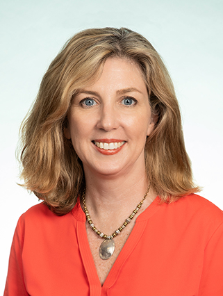 A woman with shoulder-length blonde hair, wearing a red top and a beaded necklace, smiles against a plain background.