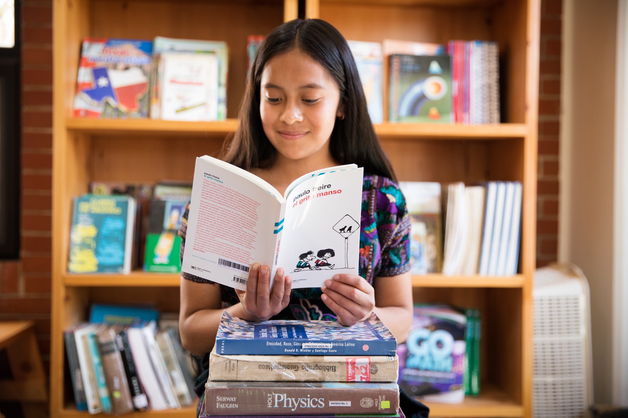 a girl reading a book in front of a stack of books.