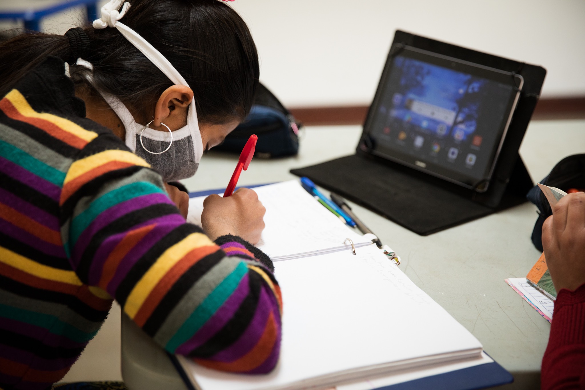 a girl wearing a face mask is writing on a tablet.