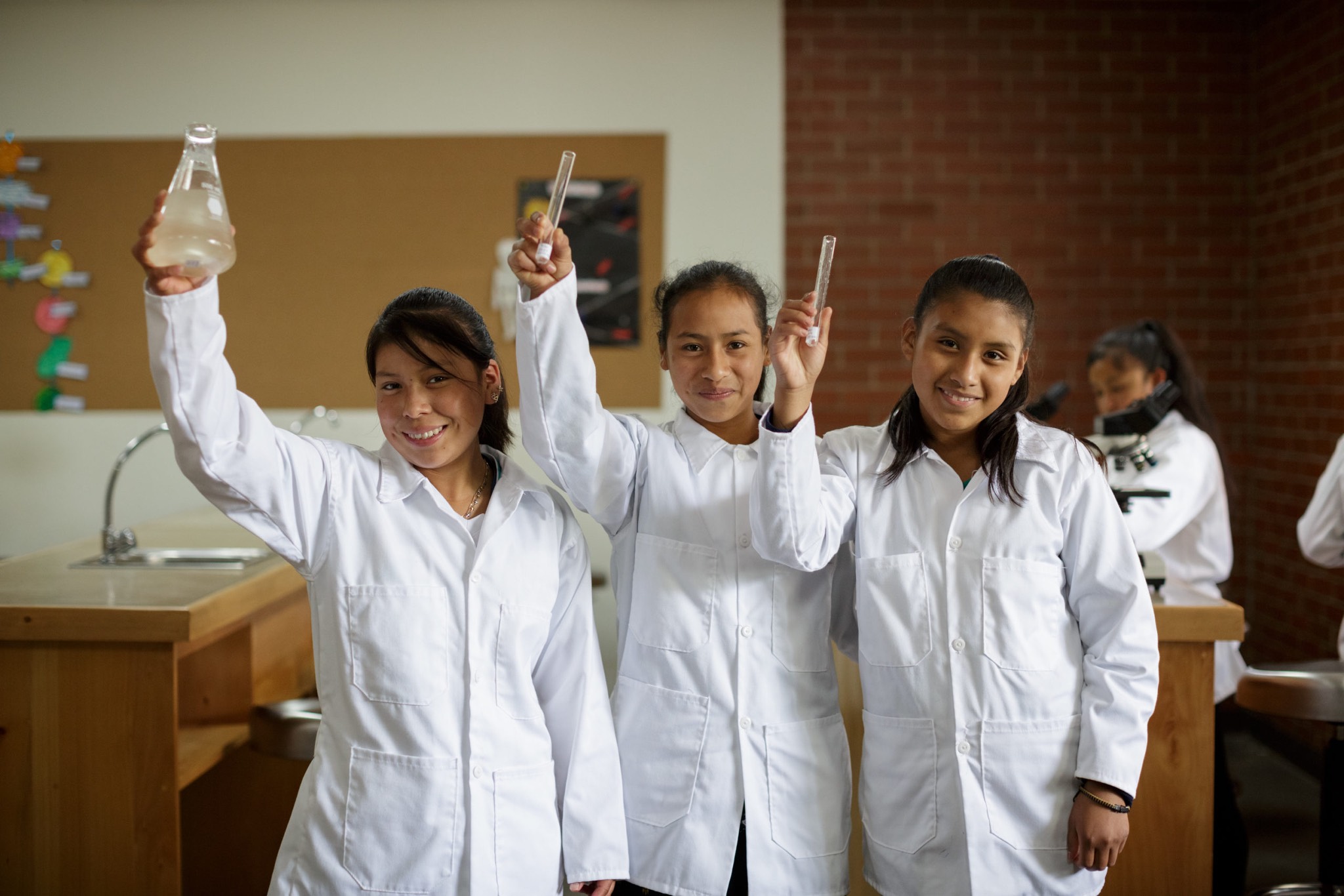 a group of girls in lab coats holding up a bottle.