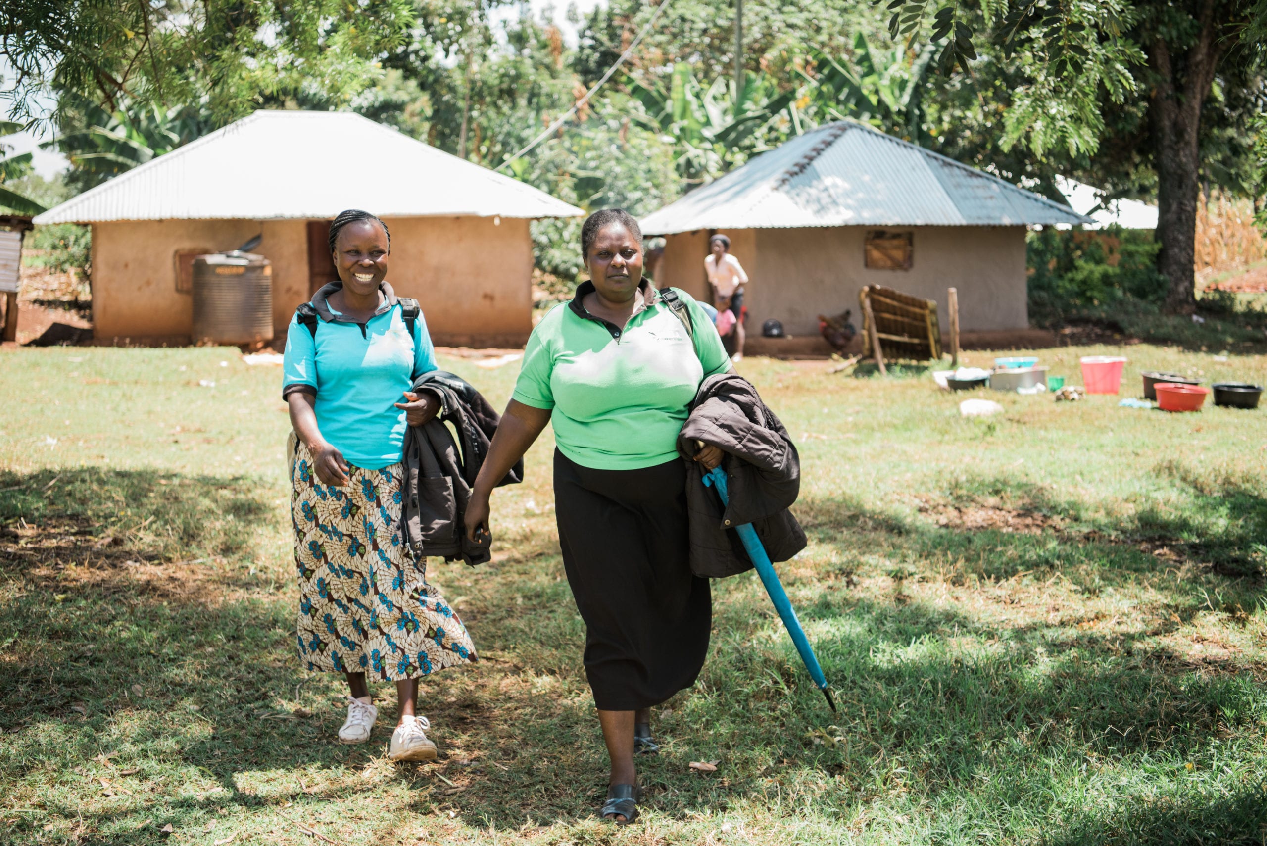 two women walking in front of a hut.