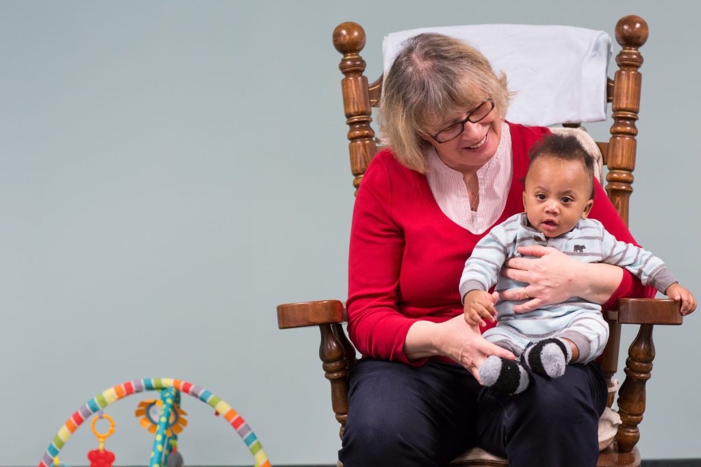 an older woman holding a baby in a rocking chair.