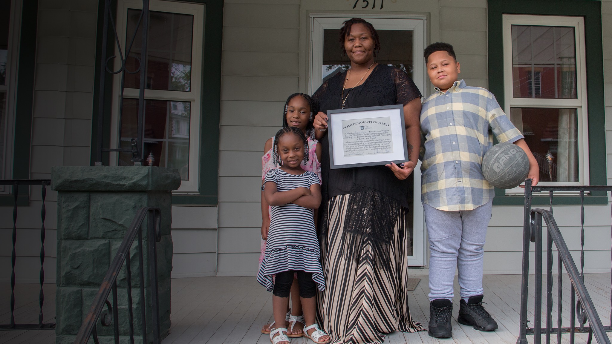 a family holding a certificate in front of their home.