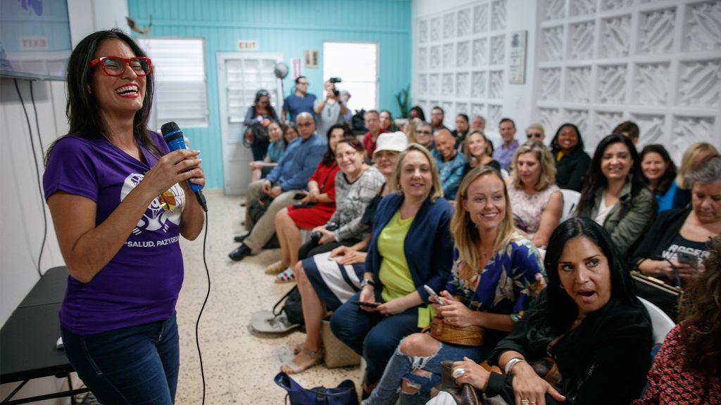 a woman in a purple shirt is speaking to an audience.