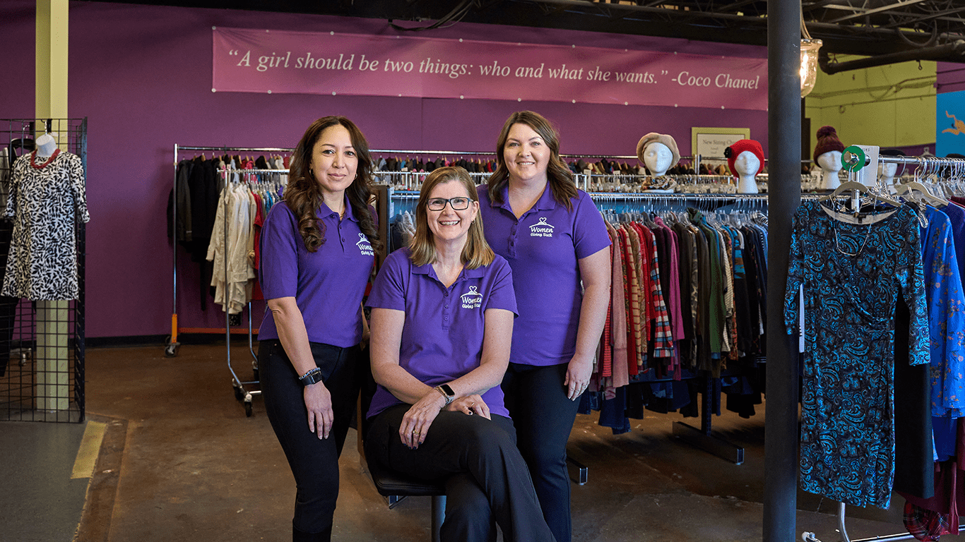three women in purple shirts standing in a clothing store.